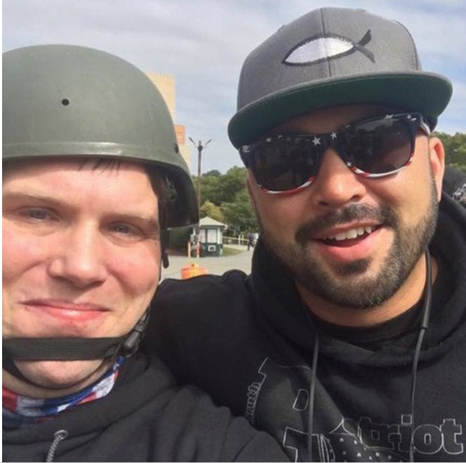Photo of John Camden wth Joey Gibson, Camden in black and wearing a gray helment, Gibson in black and sunglasses wearing a baseball hat with an ichthys or "Jesus fish" symbol.