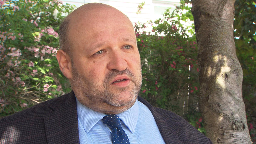 Close up photo of John Hugo, bald with grey beard in sports coat and blue tie.