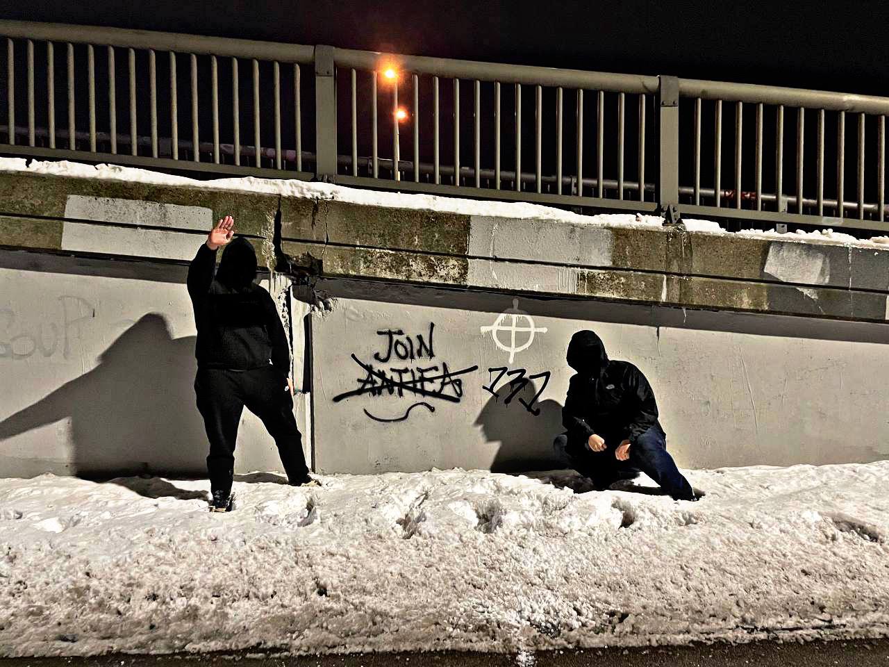 Photo of two people standing by a wall with graffiti on it. The graffiti reads: Join antifa. Antifa is crossed out 