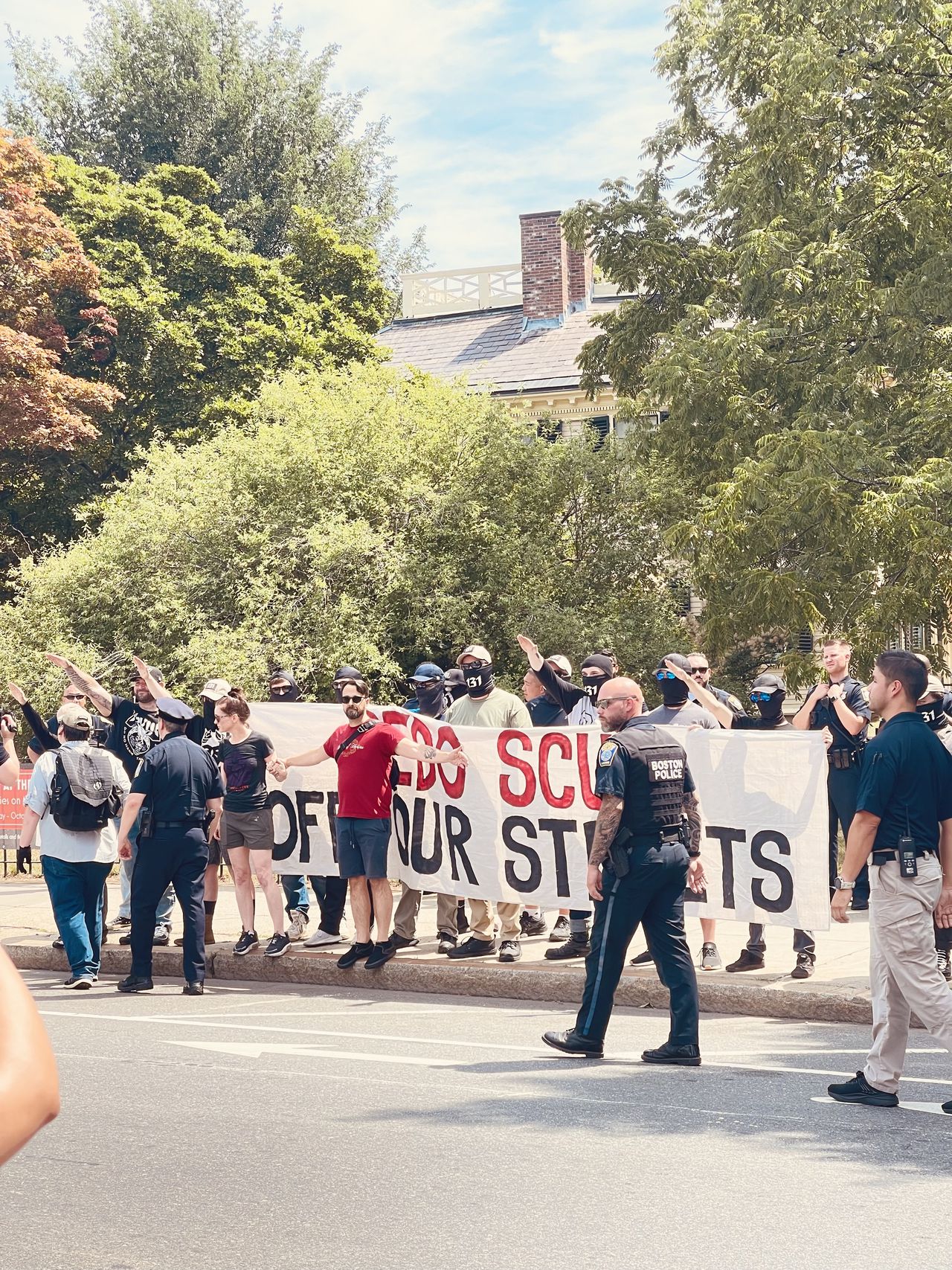 antifascist activists screen homophobic banner from view while Neo-Nazis throw up Hitler salutes